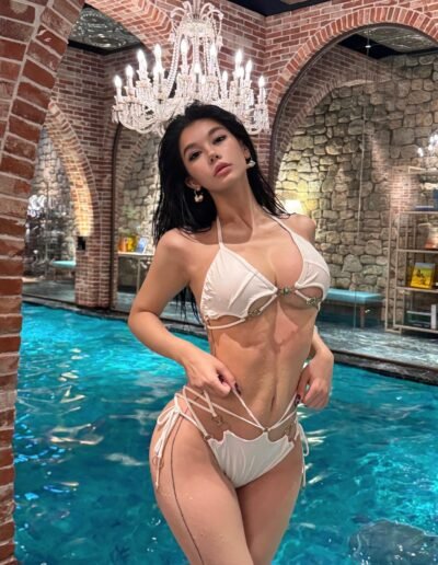 Sensual escort with long black hair, accentuating her big, sexy boobs in a seductive pose.
